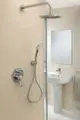 Duscharmatur mit Handbrause und Kopfbrause, verchromt, an grauer Wand, daneben ein Waschbecken mit modernem Wasserhahn, Badezimmer von Ideal Standard.